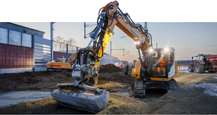 Markgraf-Bagger bei Erdarbeiten im Gleisbereich während der Dämmerung, mit Baustellenbeleuchtung